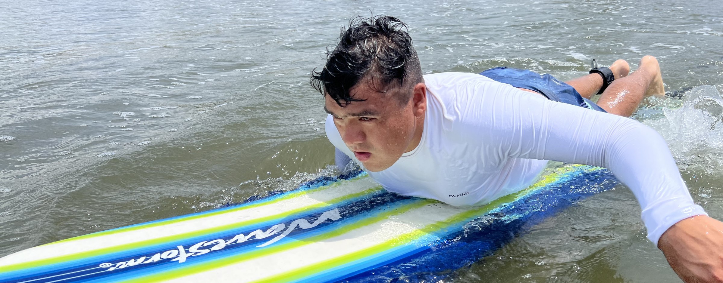 Alumno remando sobre una tabla de foam hacia la cámara durante una clase de surf en San Blas
