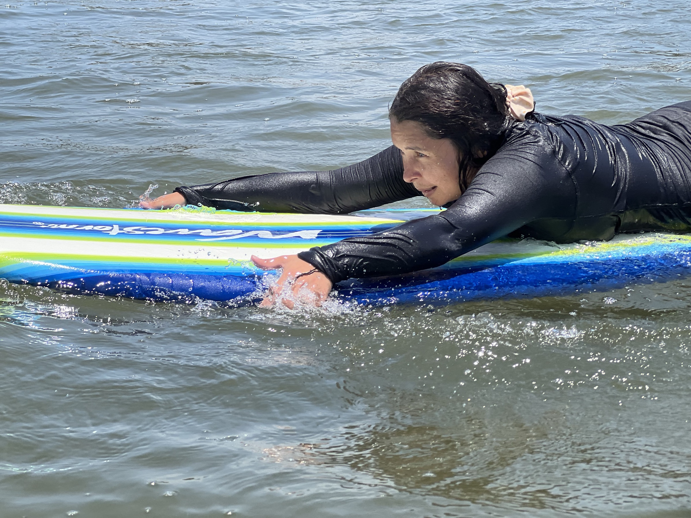 Alumna remando acostada sobre una tabla larga, con el agua salpicando alrededor