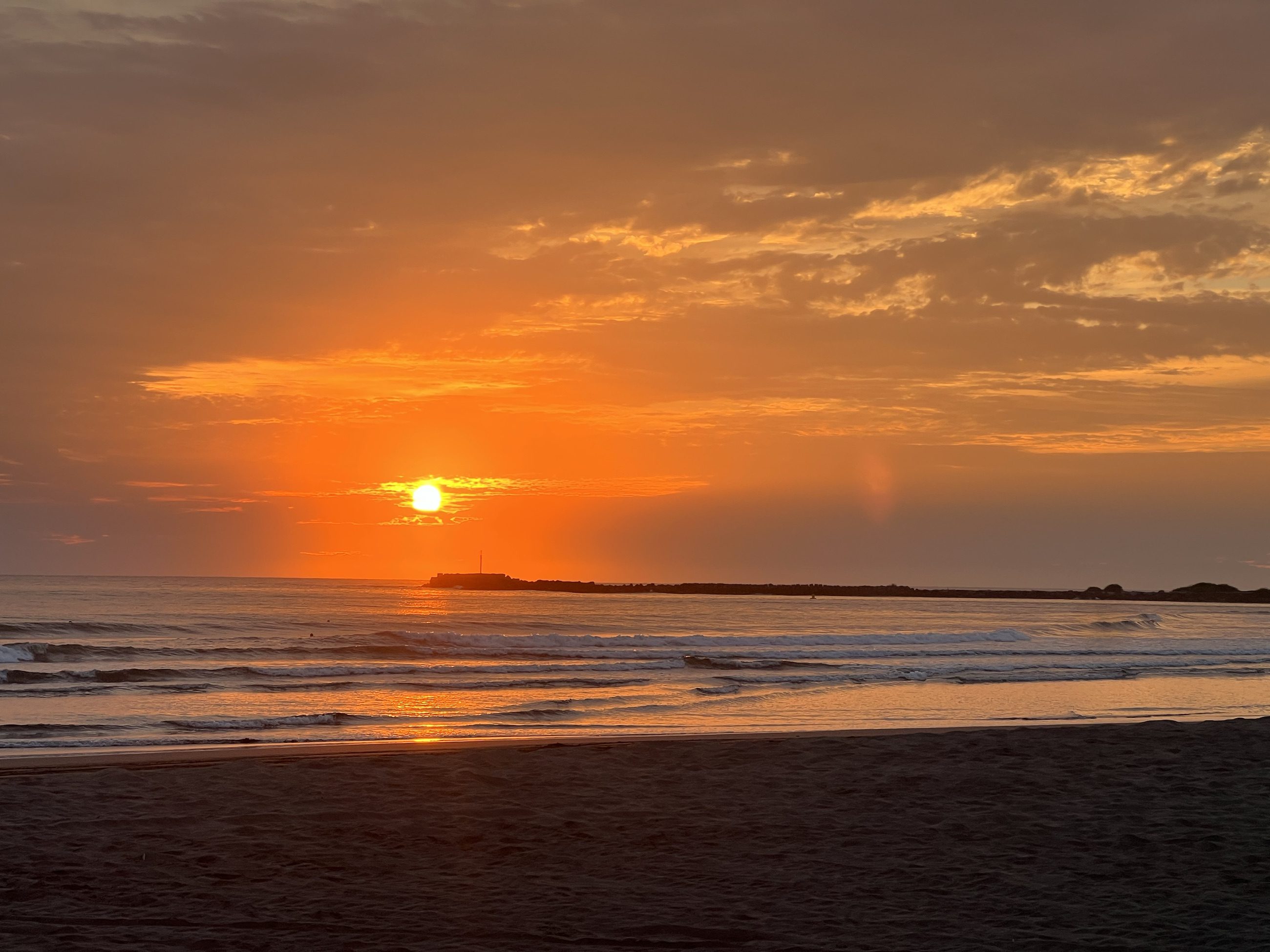 Sol dorado bajo sobre el agua y la arena oscura